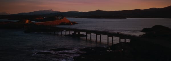Verschwommene Küstenlandschaft mit einer Brücke bei Sonnenuntergang.