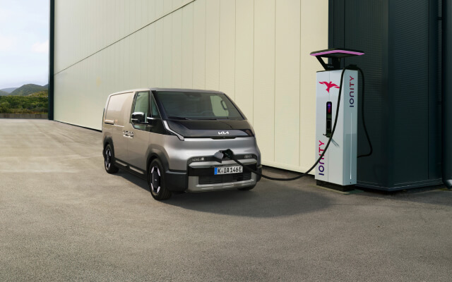 Vorderansicht des Kia PV5 Passenger, verbunden mit einer Ladestation, mit sichtlicher Darstellung des Antriebsstrangs.